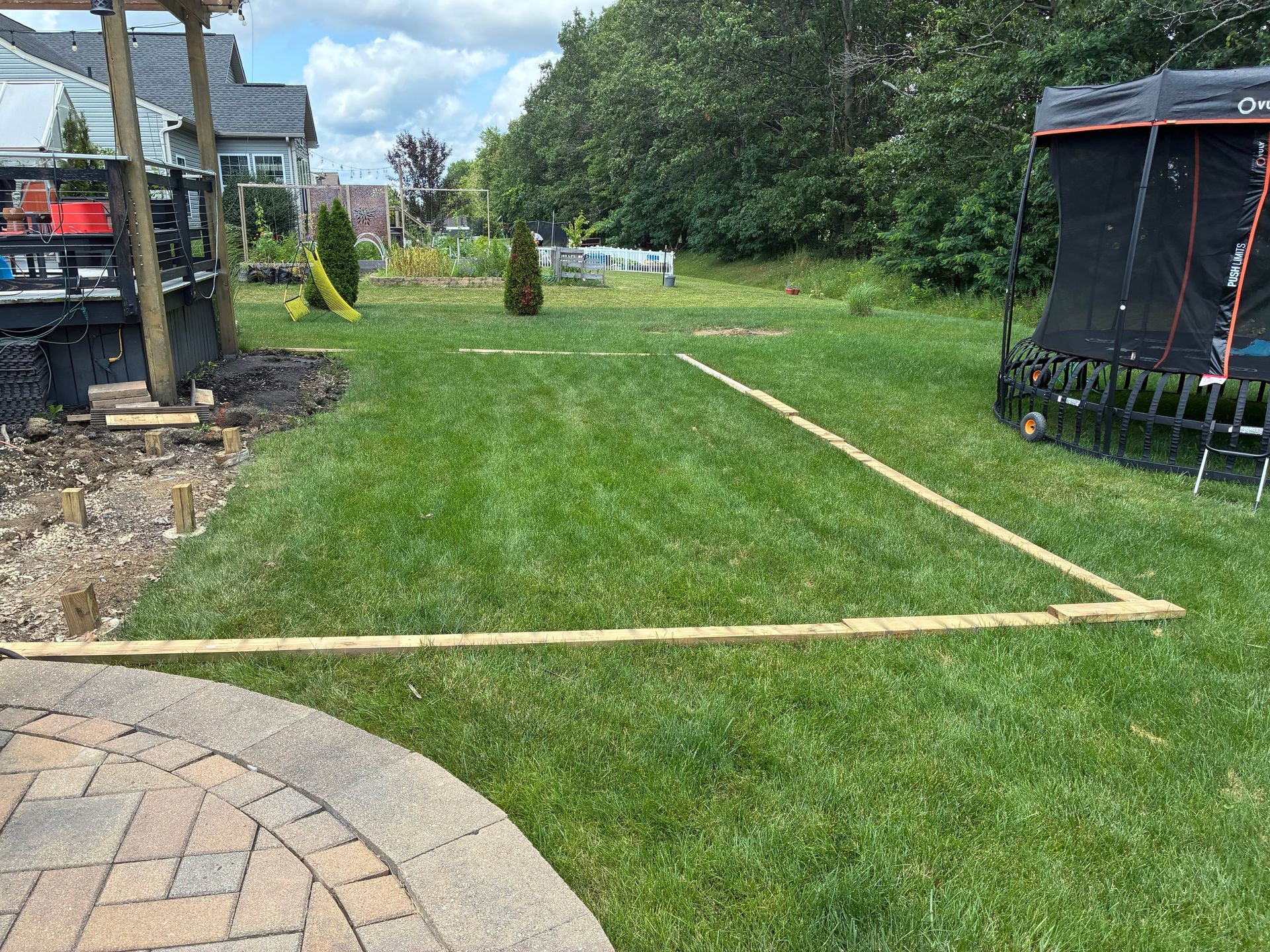 Green grass with wooden beams outlining a rectangular area in a backyard setting.
