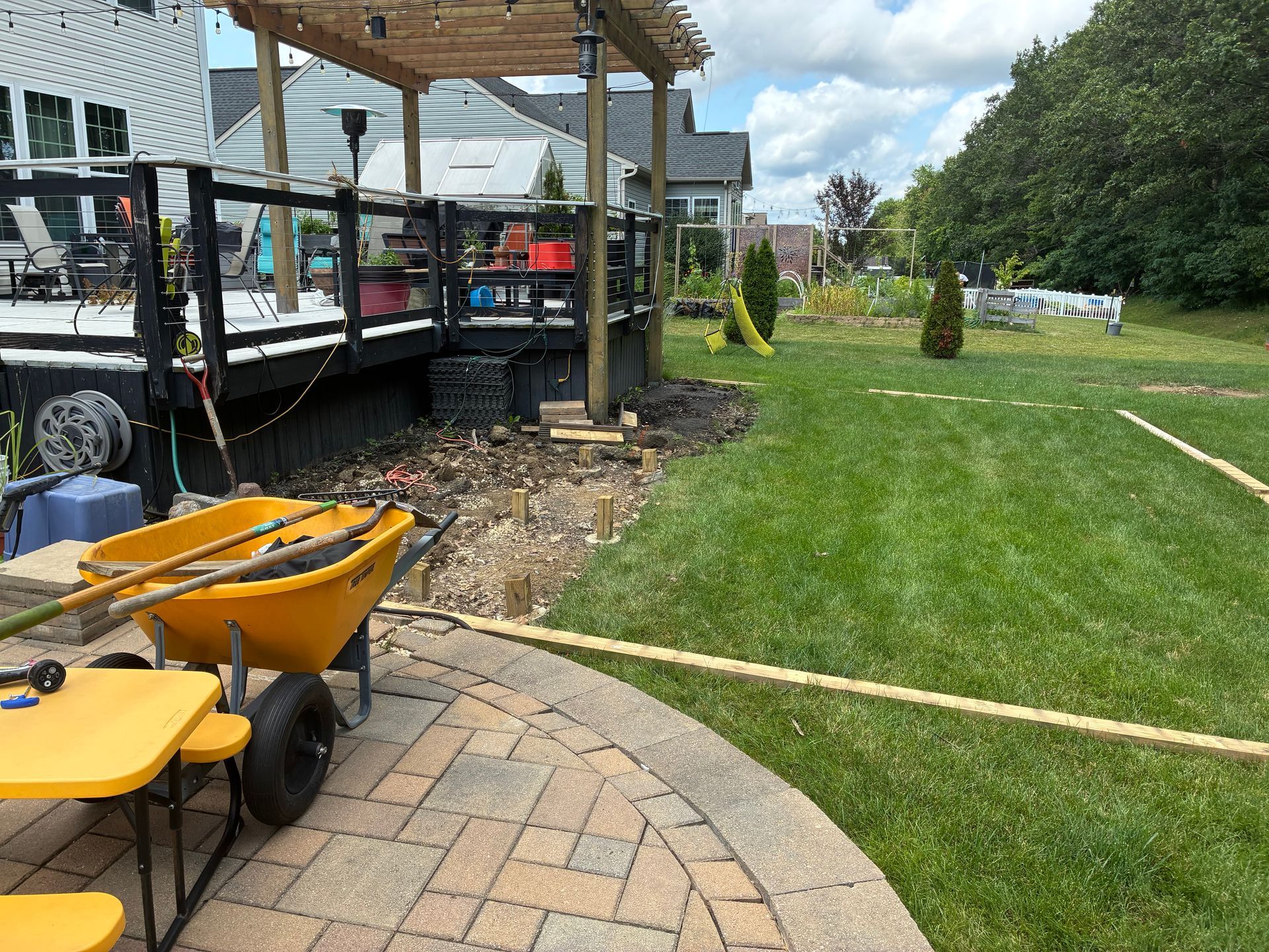 Backyard with deck and landscaping in progress; wheelbarrow, patio, and lawn.