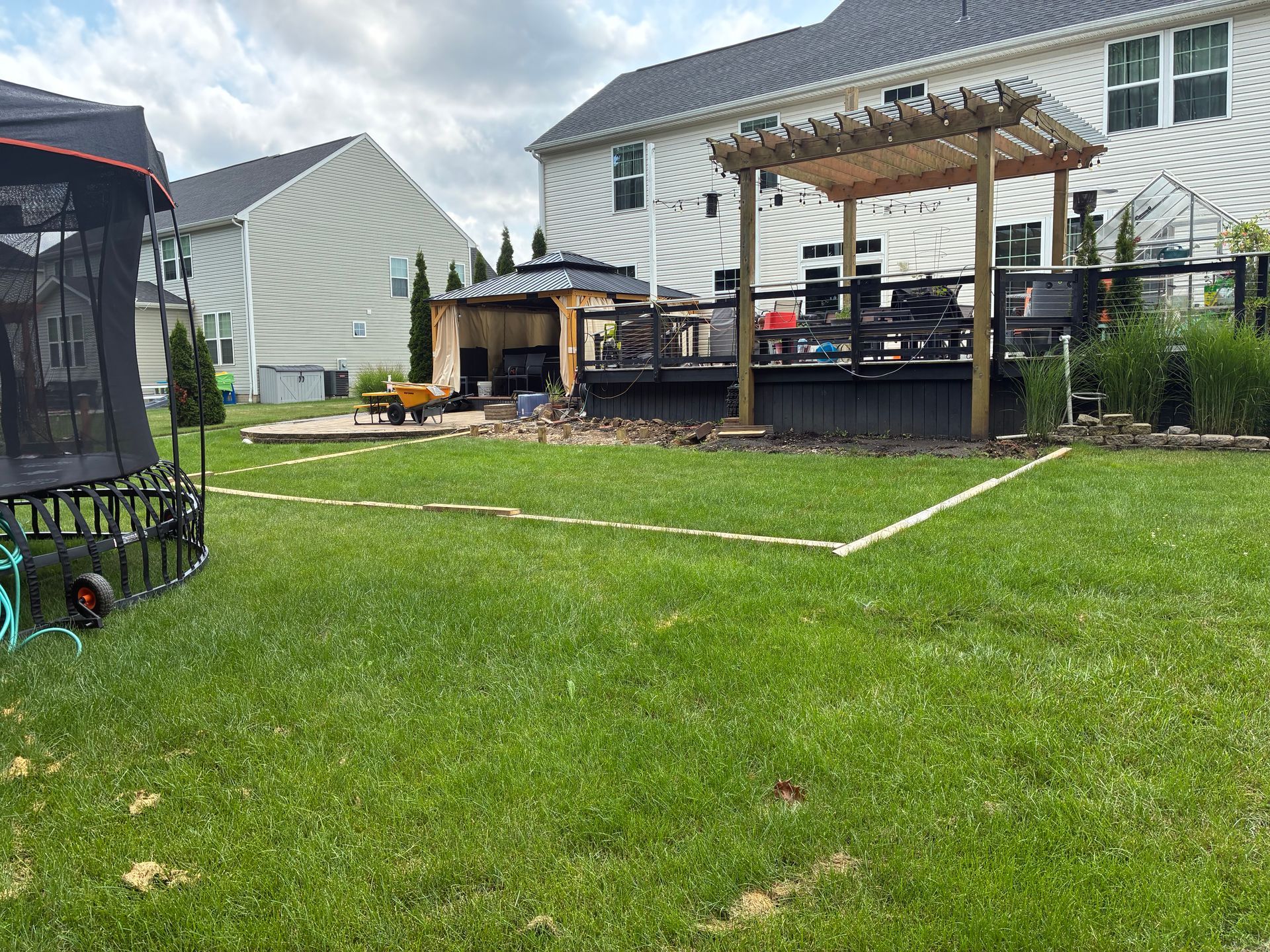 Backyard with grass, deck, gazebo, and trampoline; white outline on lawn.