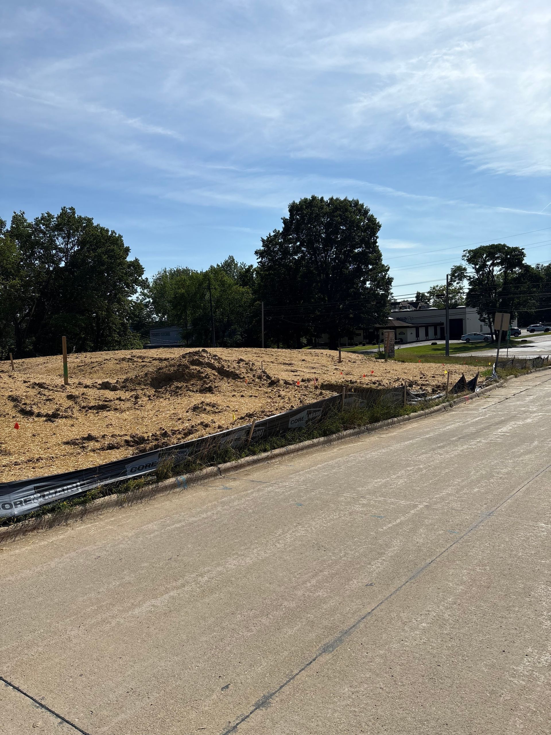 Cleared vacant lot covered in mulch next to a paved road, under a blue sky.