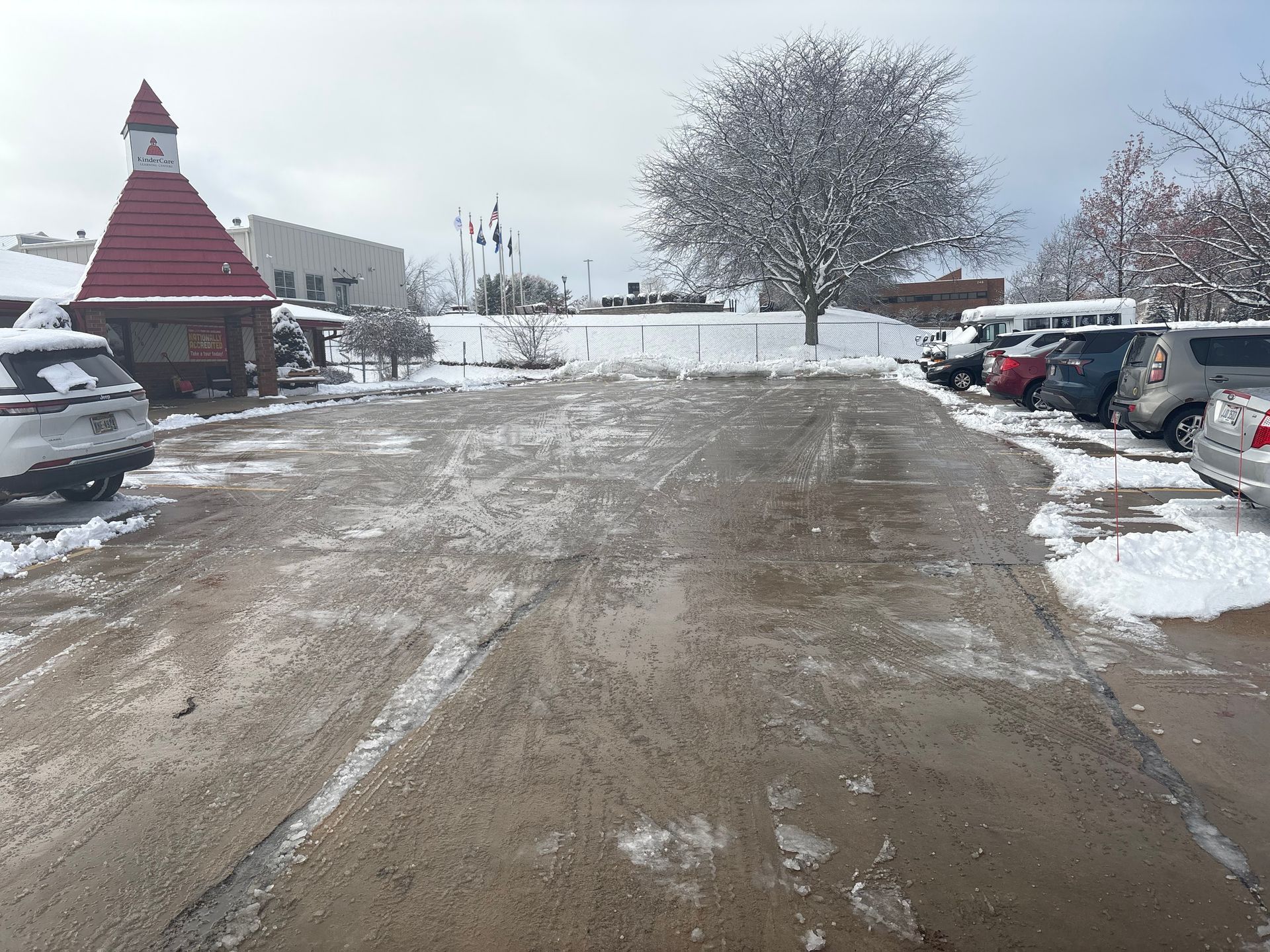 Snowy parking lot with cars and a building featuring a red roof and a small tower.