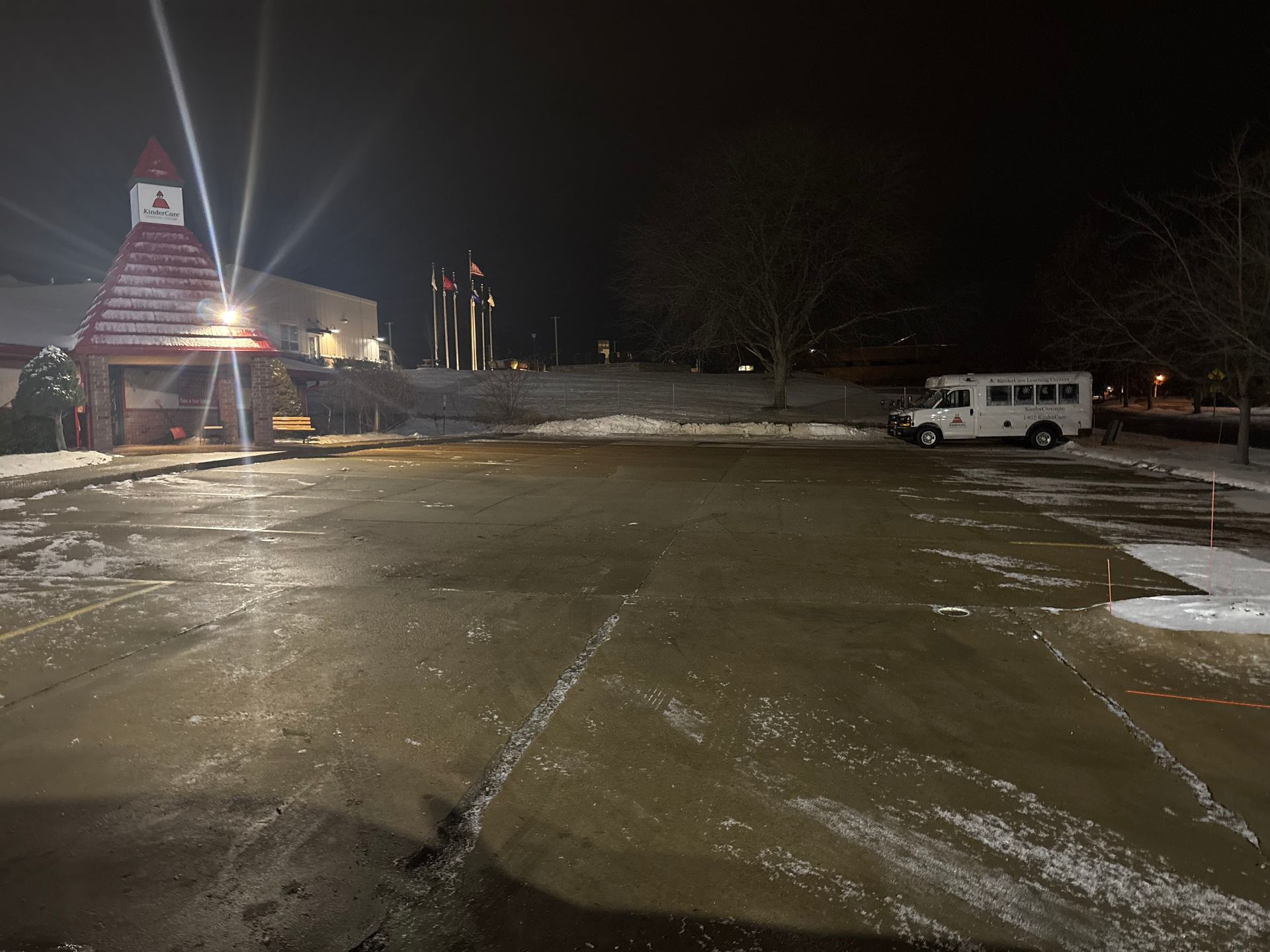 Dark, snowy parking lot with a white van, and building with a red roof at night.