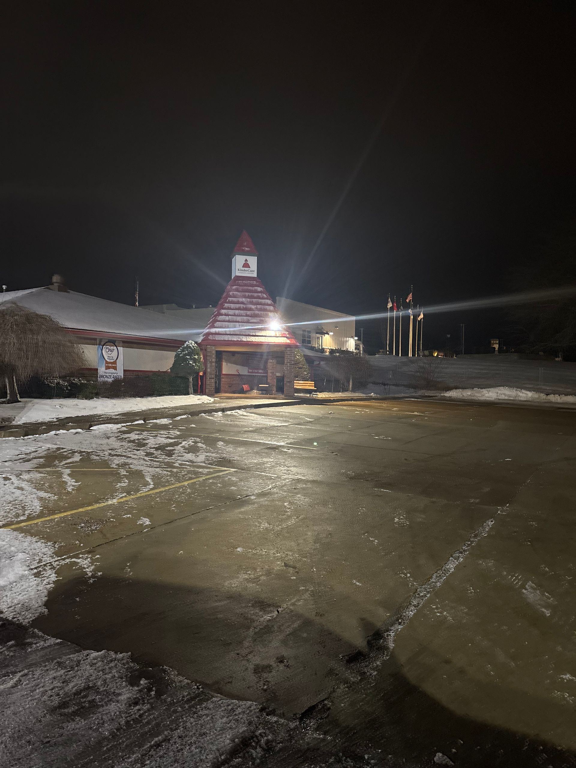 A building with a red-roofed tower, snowy parking lot, at night.