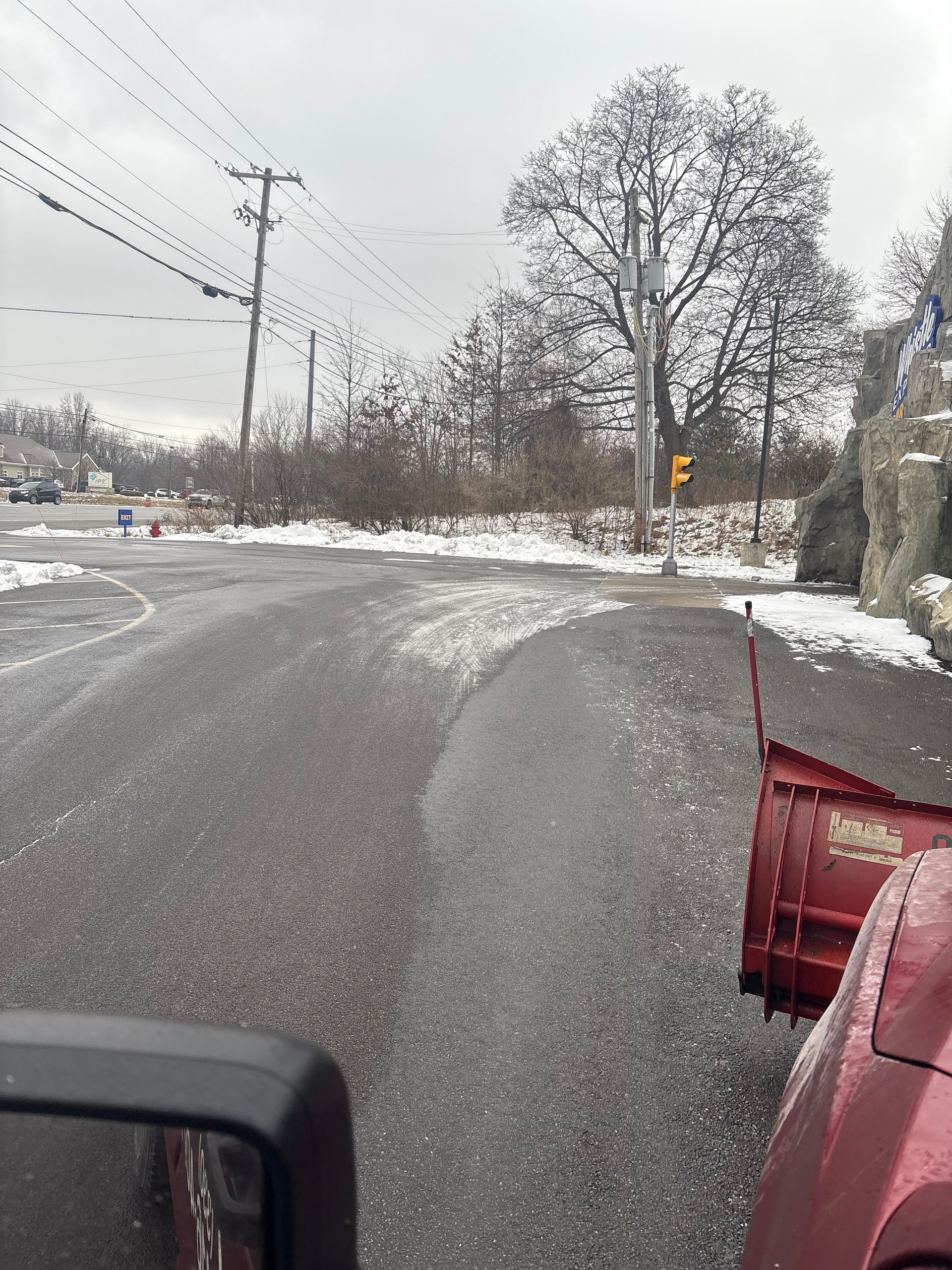 Snowplow clears a road during winter. Gray sky, leafless trees, snow on the ground.