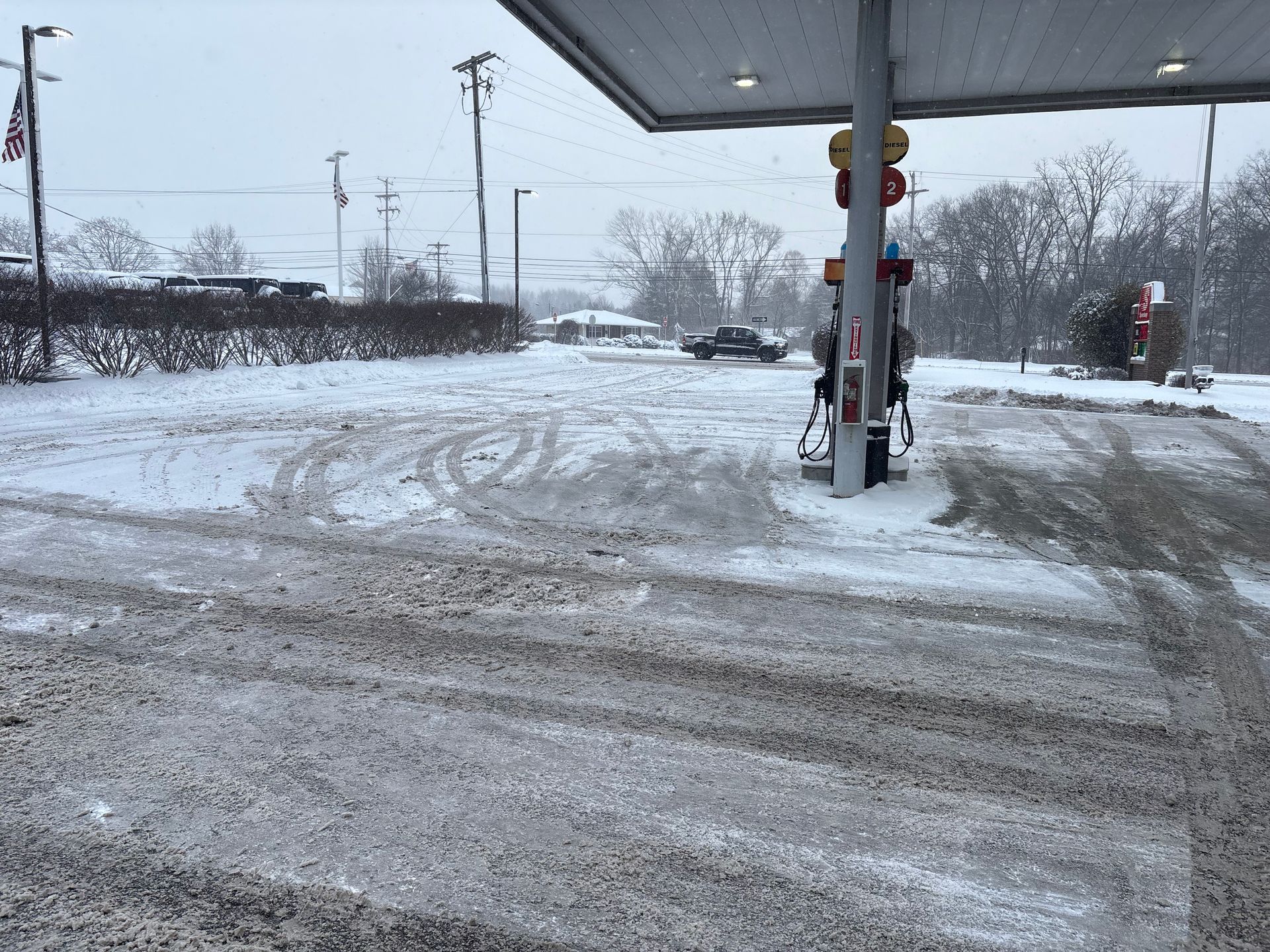 Snowy gas station scene. Snow covers the ground and the pump, with a vehicle in the distance.