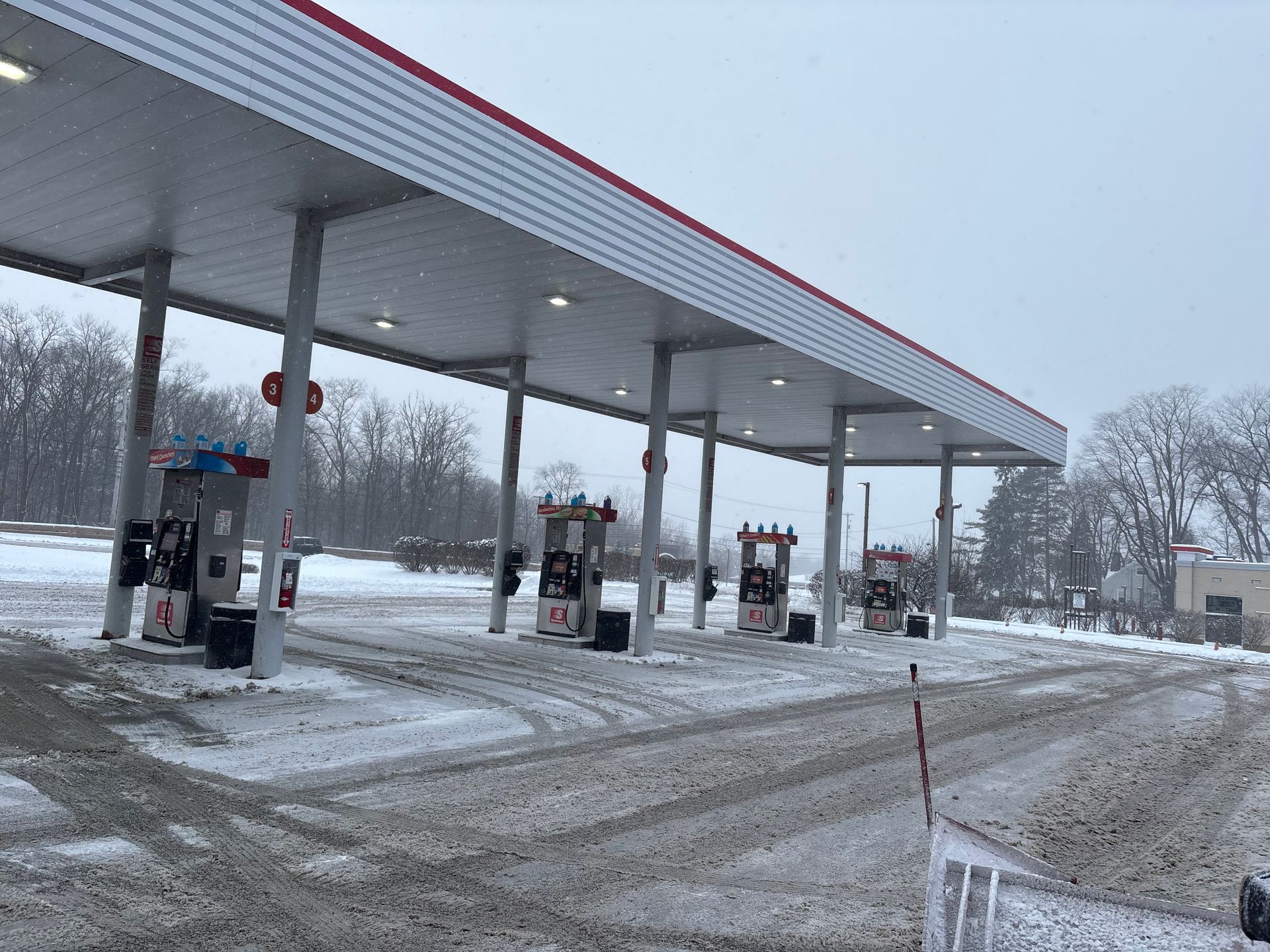Gas station in winter; snow covers the pumps and ground under a canopy.