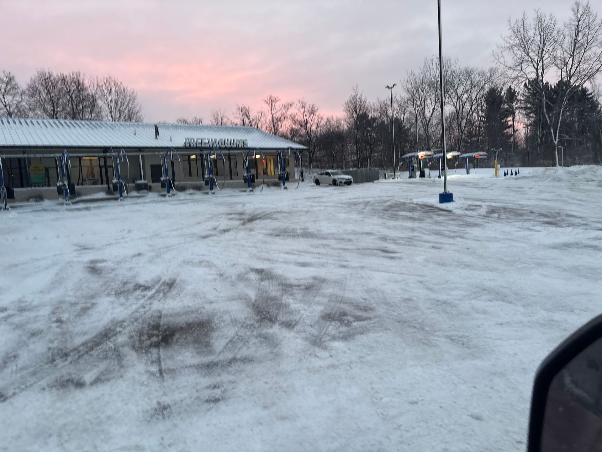 Snow-covered car wash at dusk. Pink sky above a building with open bays and a parked car.