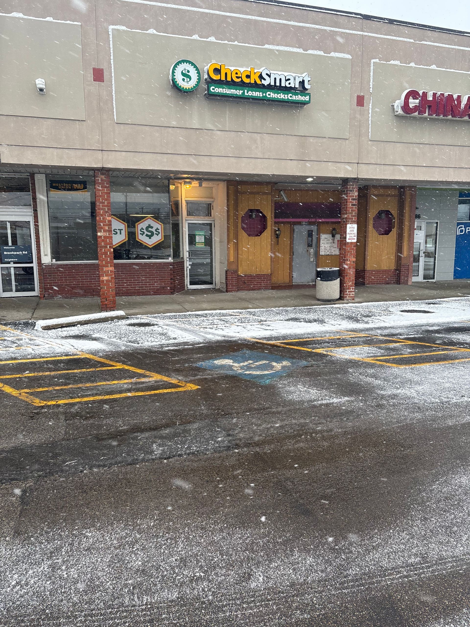 Snowy day at a strip mall. Check Smart and China Wok storefronts visible. Gray pavement.