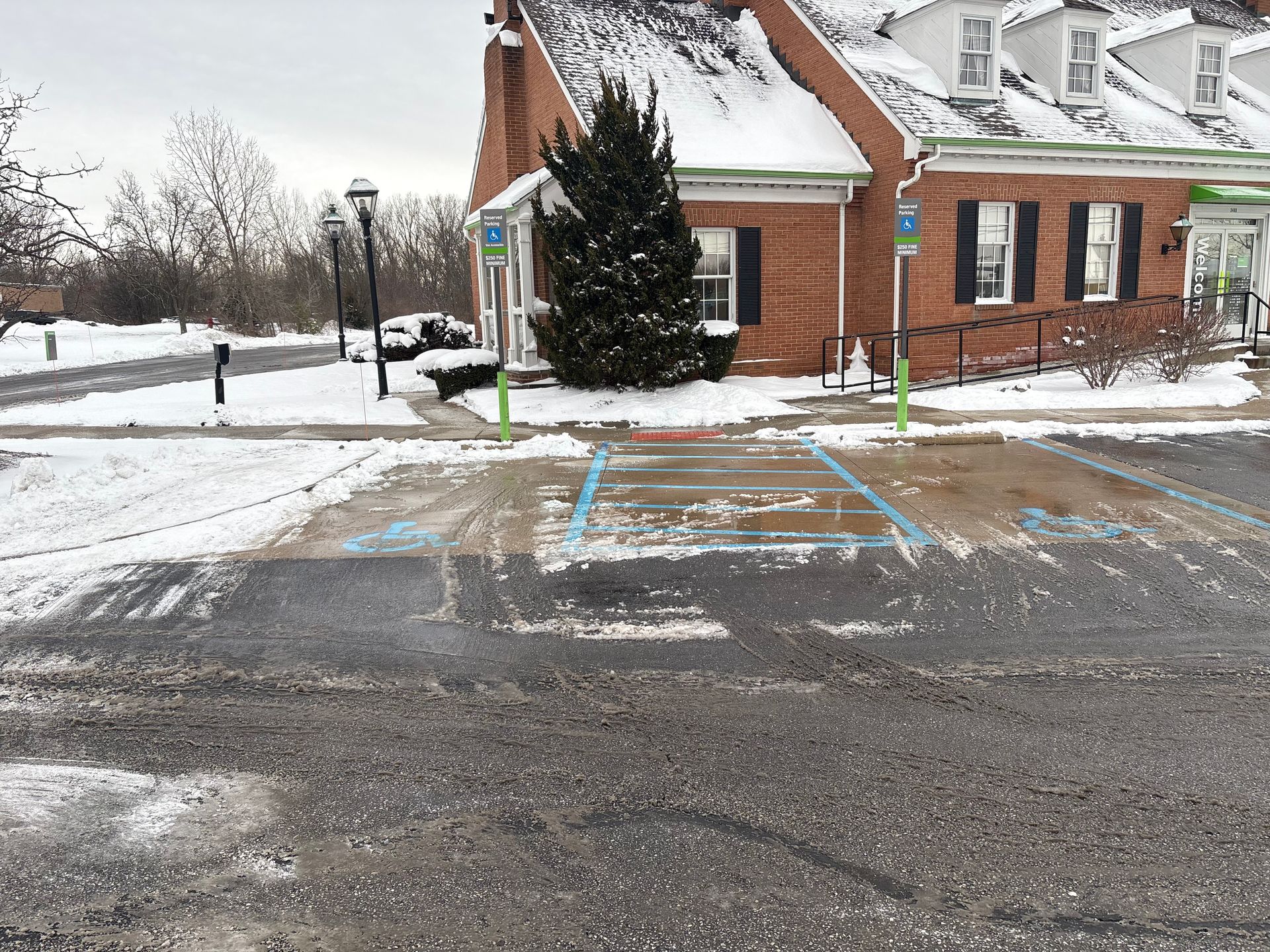 Snowy parking lot with accessible parking spots in front of a brick building.