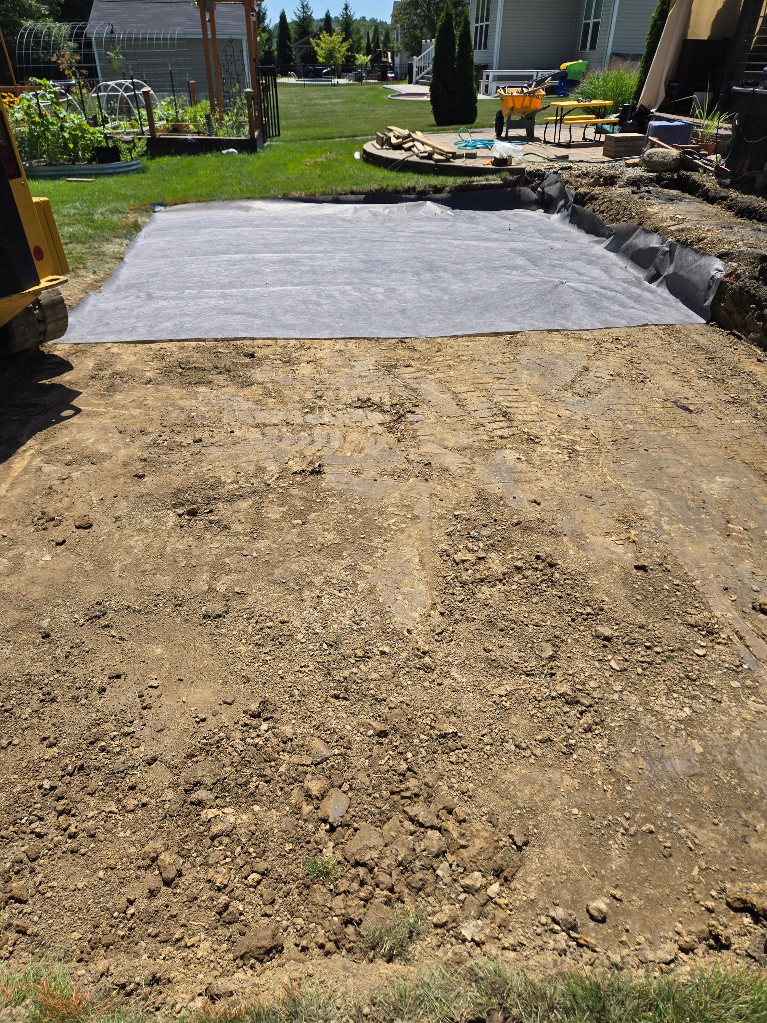 A backyard with a prepared area for paving, covered in landscape fabric; dirt is visible.