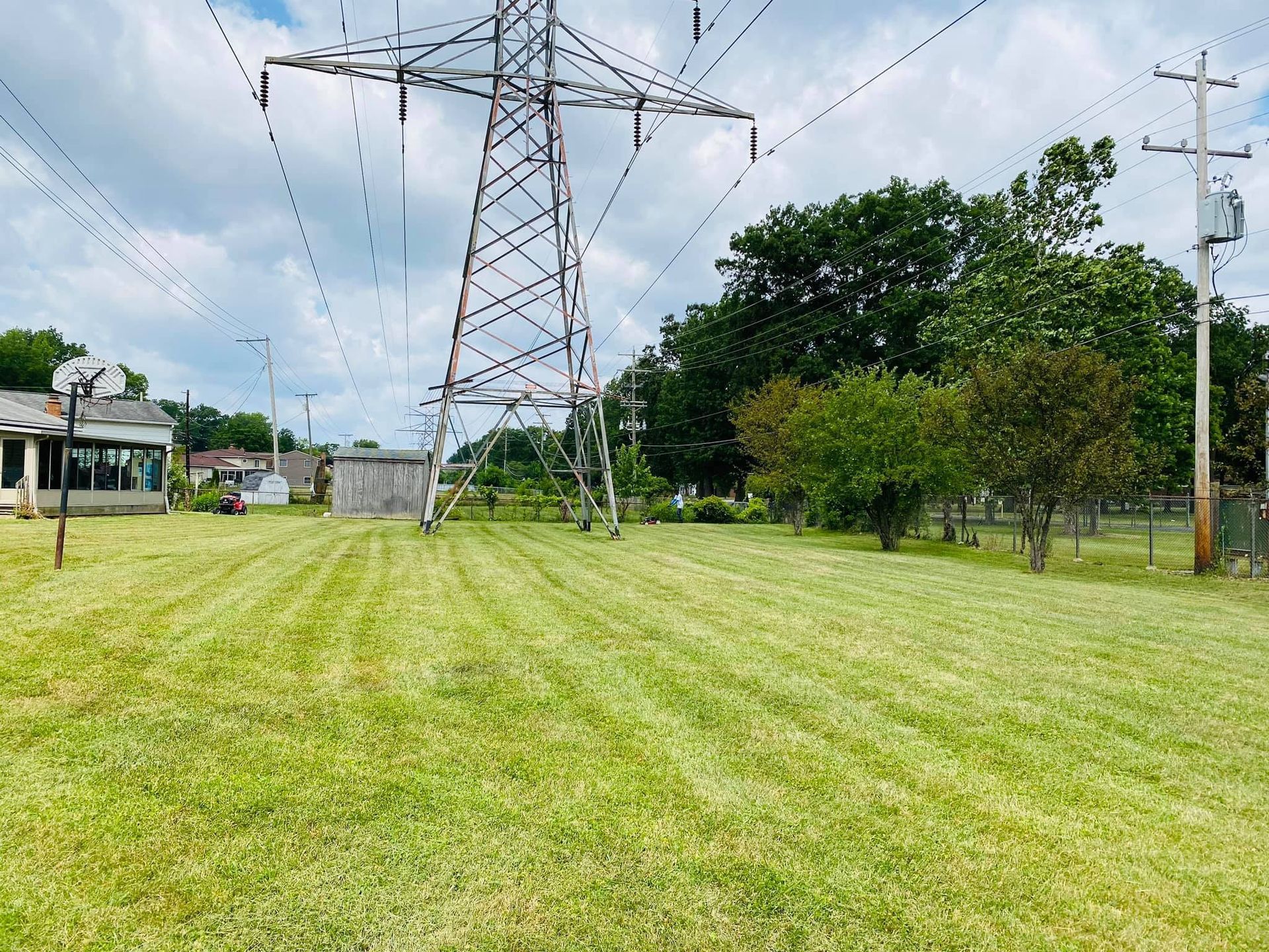 Green field with freshly cut grass, power lines and a utility pole. Cloudy sky.