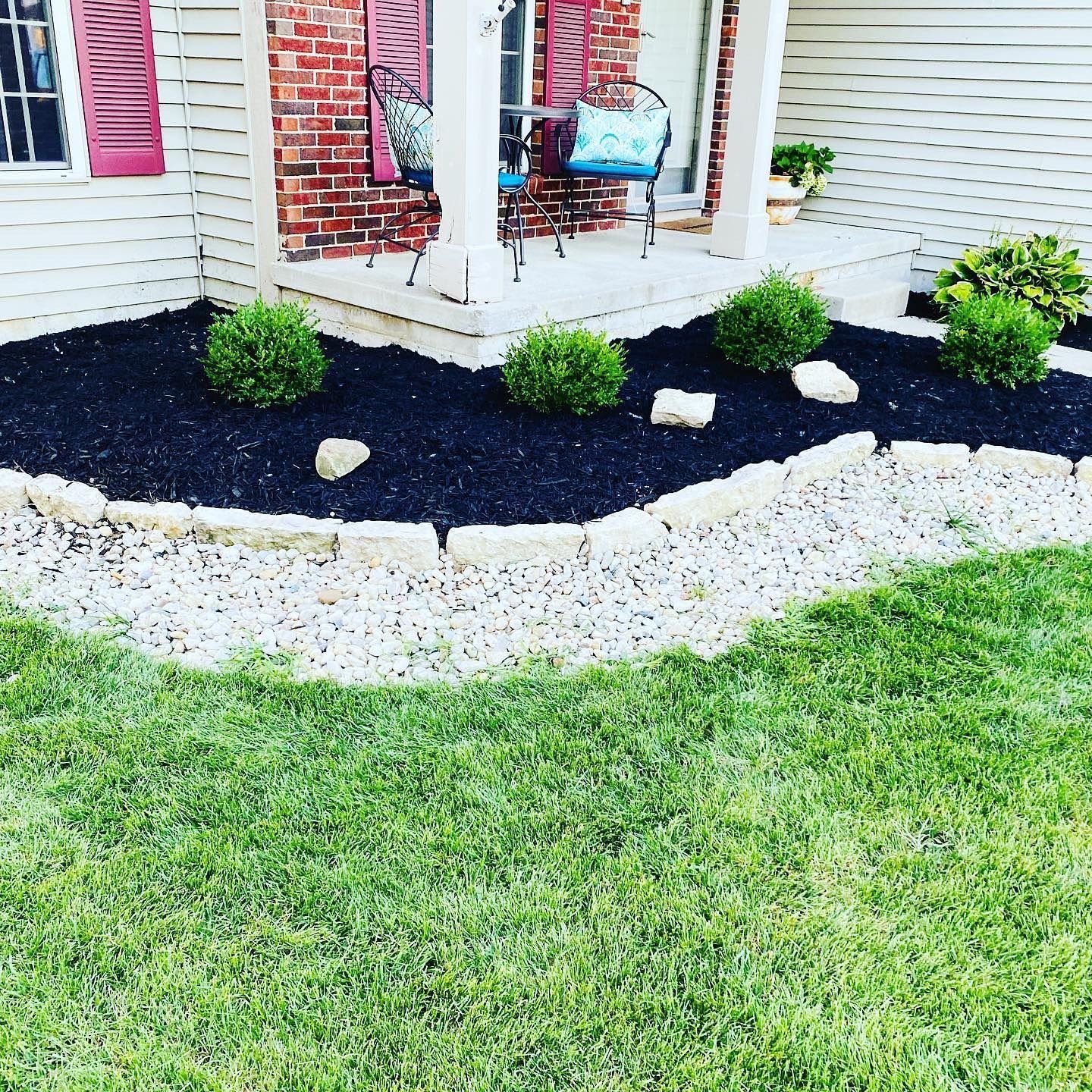 Front yard flower bed with dark mulch, rounded green shrubs, and white stone border.
