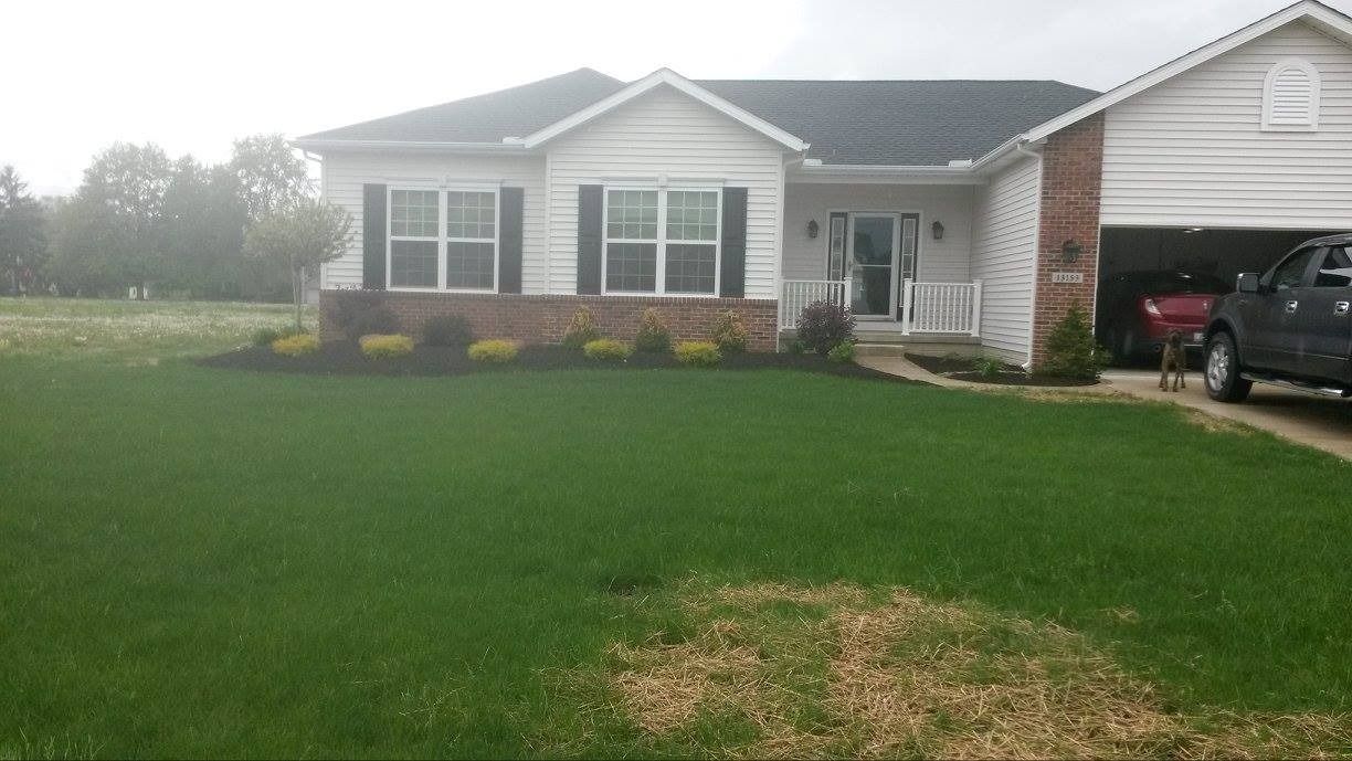 A white house with a brick facade and black shutters, a garage, and a truck parked in the driveway.