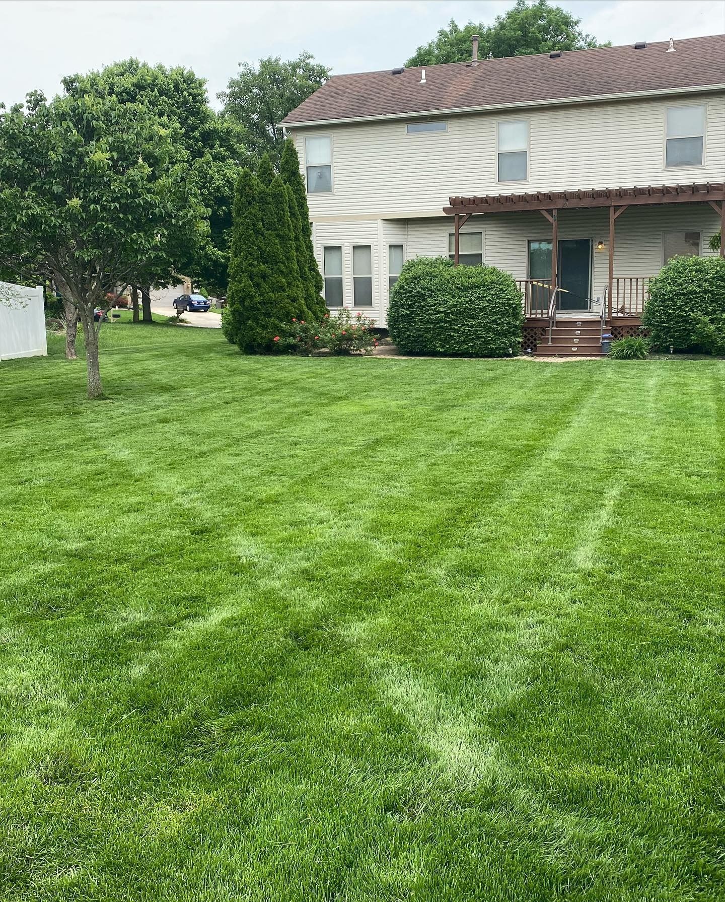 Green lawn in front of a two-story house with a wooden pergola.