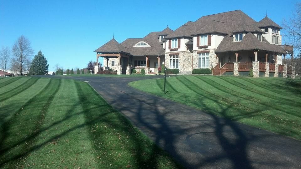 Large house with a long driveway and striped green lawn under a blue sky.