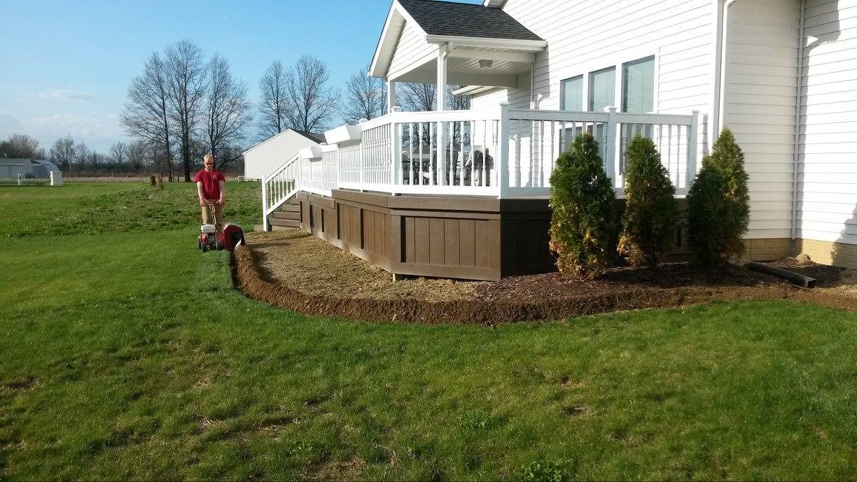 Person mowing grass near a house with a deck and landscaping.