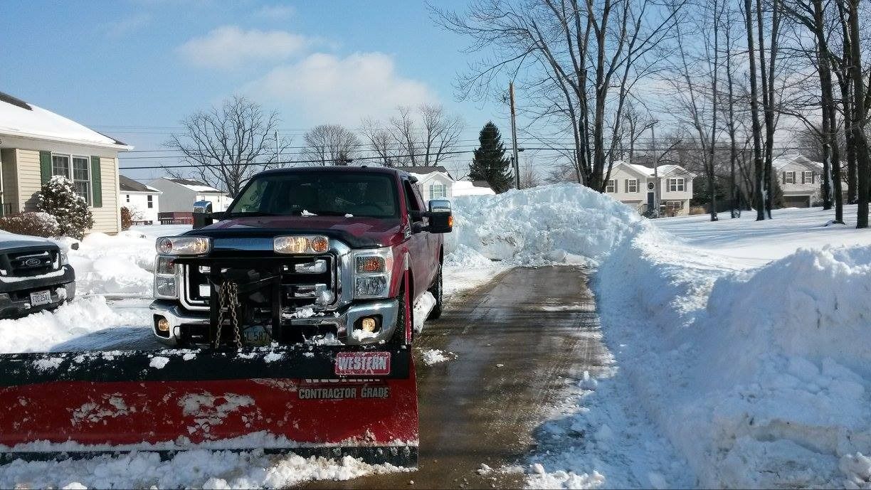 Red snowplow clearing a snow-covered residential street on a sunny day.