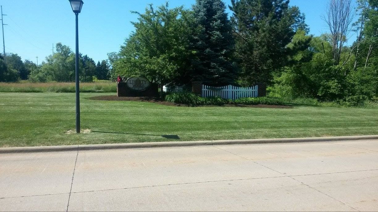 Grassy area with a white picket fence, trees, and a street lamp on a sunny day.