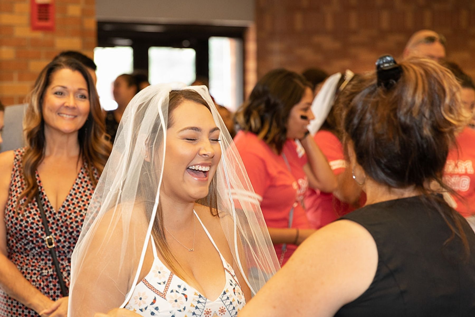 bride in line laughing with wedding veil on with other woman at wedding festival