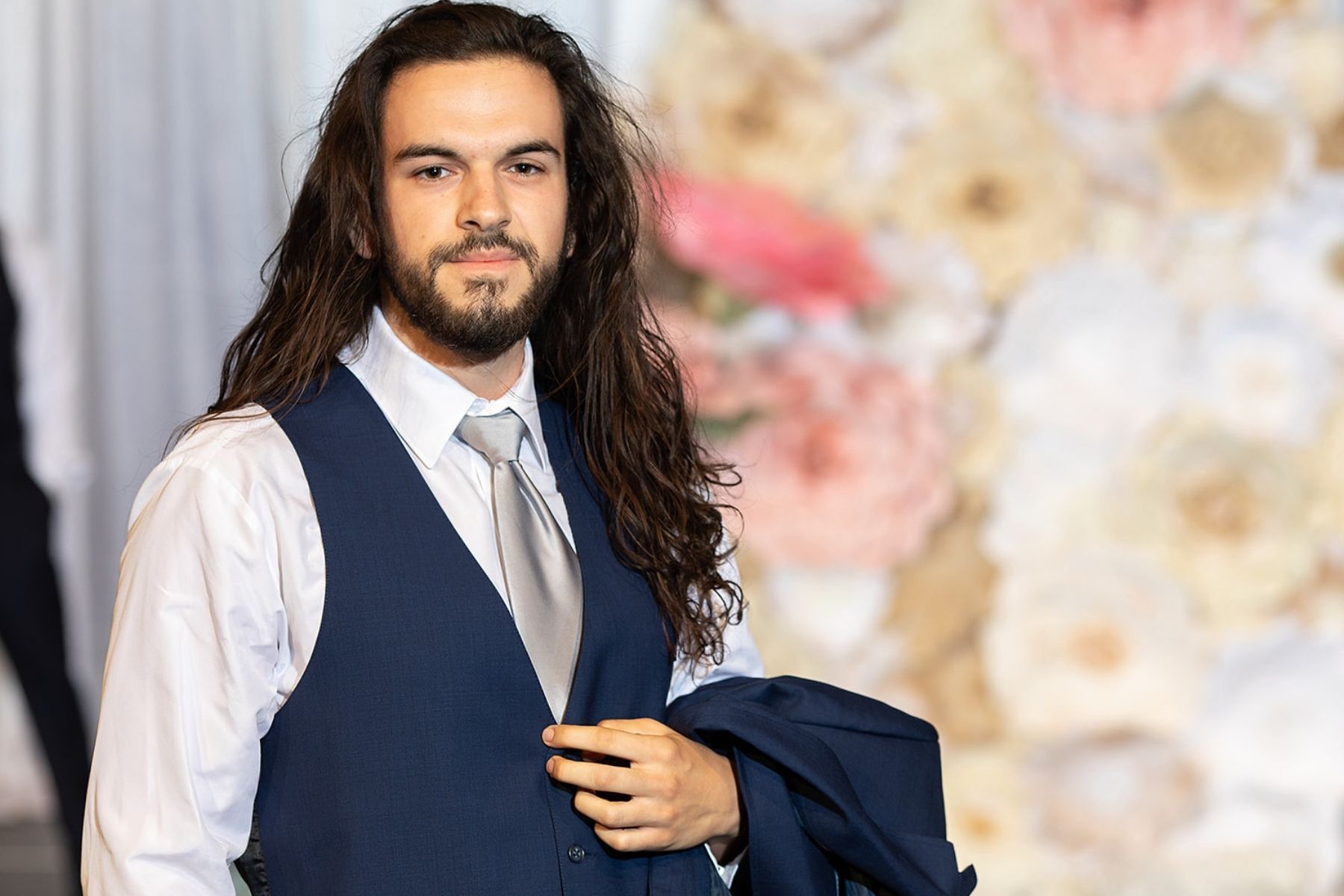 man with long hair wearing dark blue tux with gray tie and white shirt on runway at bridal show