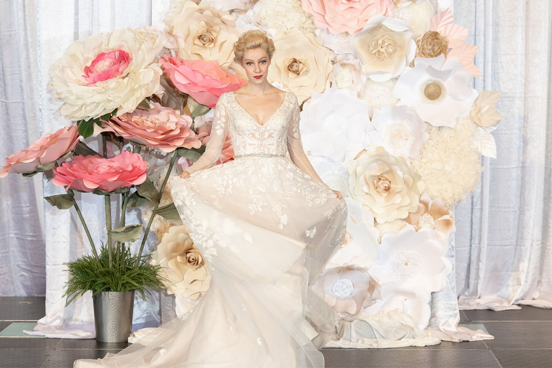 model in wedding gown at fresno bridal show with pink flowers, white flowers and flower wall on runway