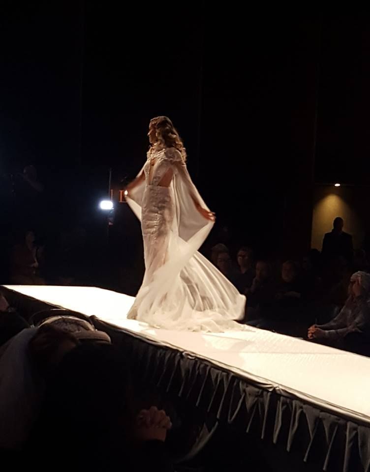 A woman in a white dress is walking down a runway