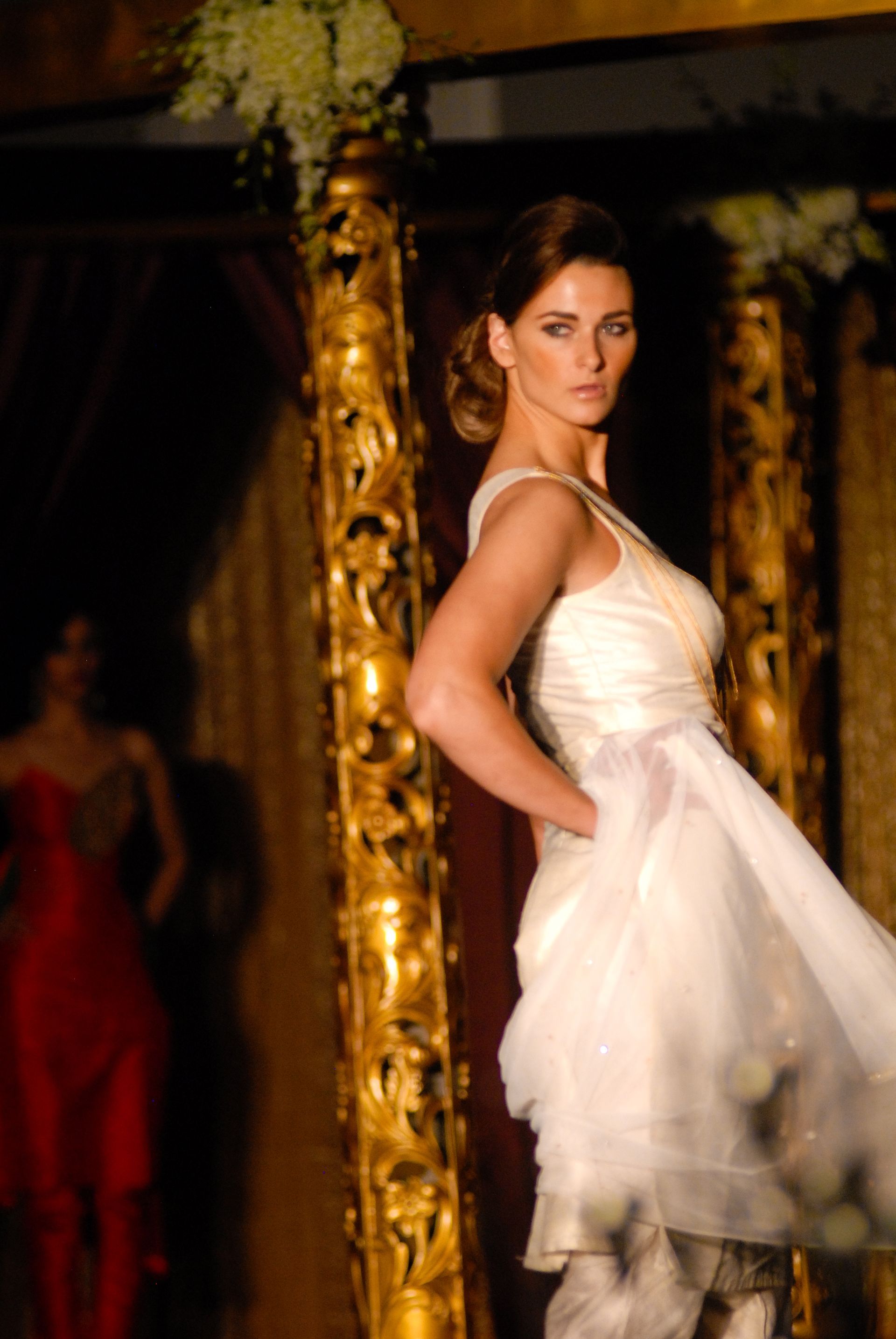 A woman in a white dress is walking down a runway