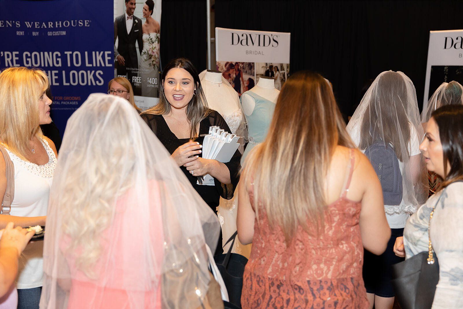 A group of women are standing in a room talking to each other.