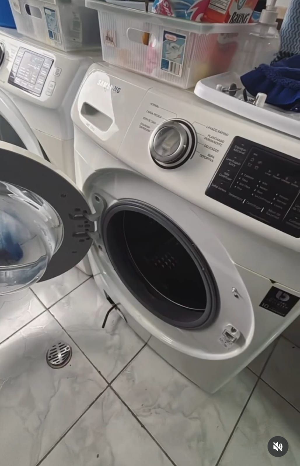 Hombre arrodillado, arreglando una lavadora en una cocina, utilizando una herramienta.