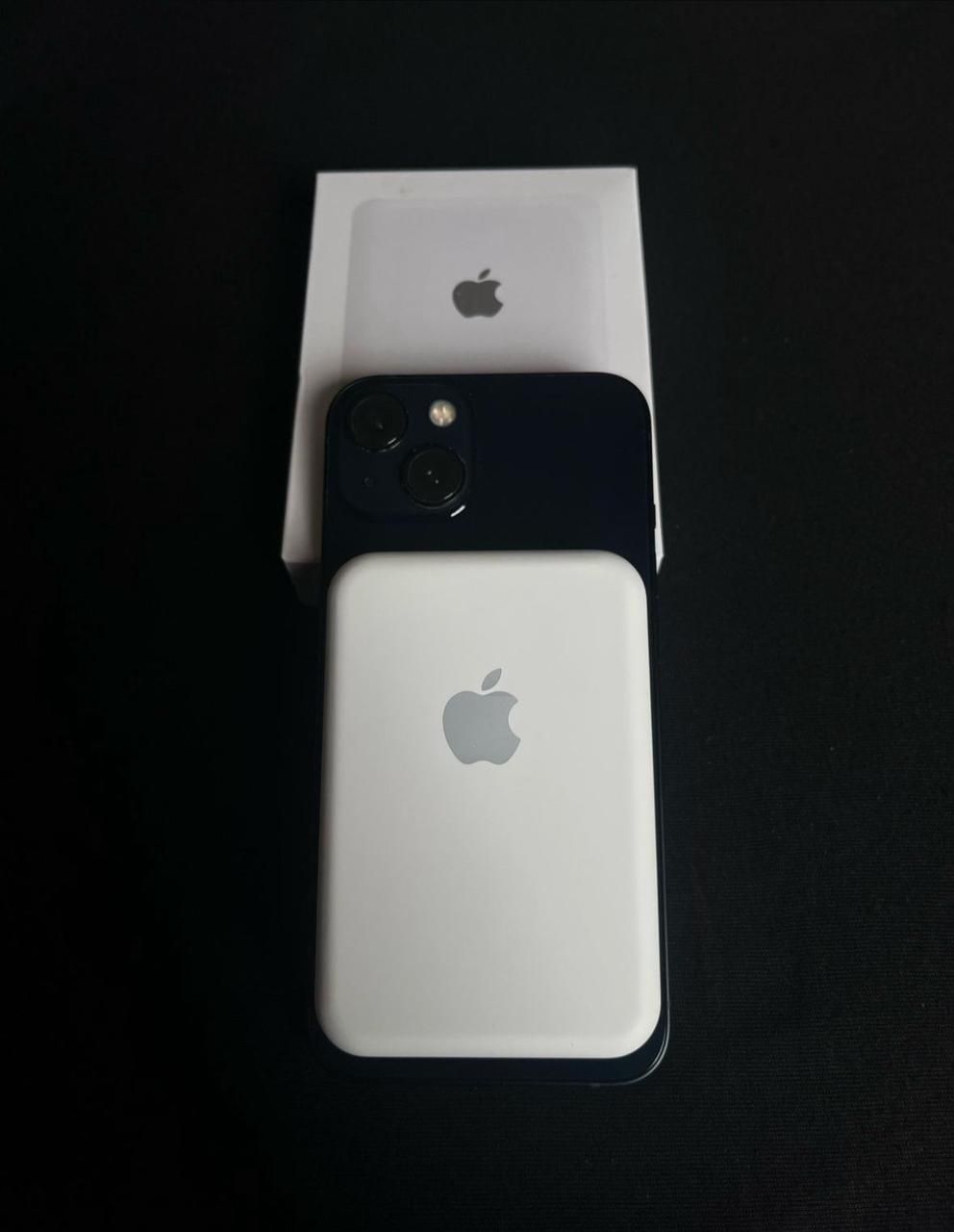 IPhone blanco con cámara negra, junto a su caja, sobre una superficie negra.