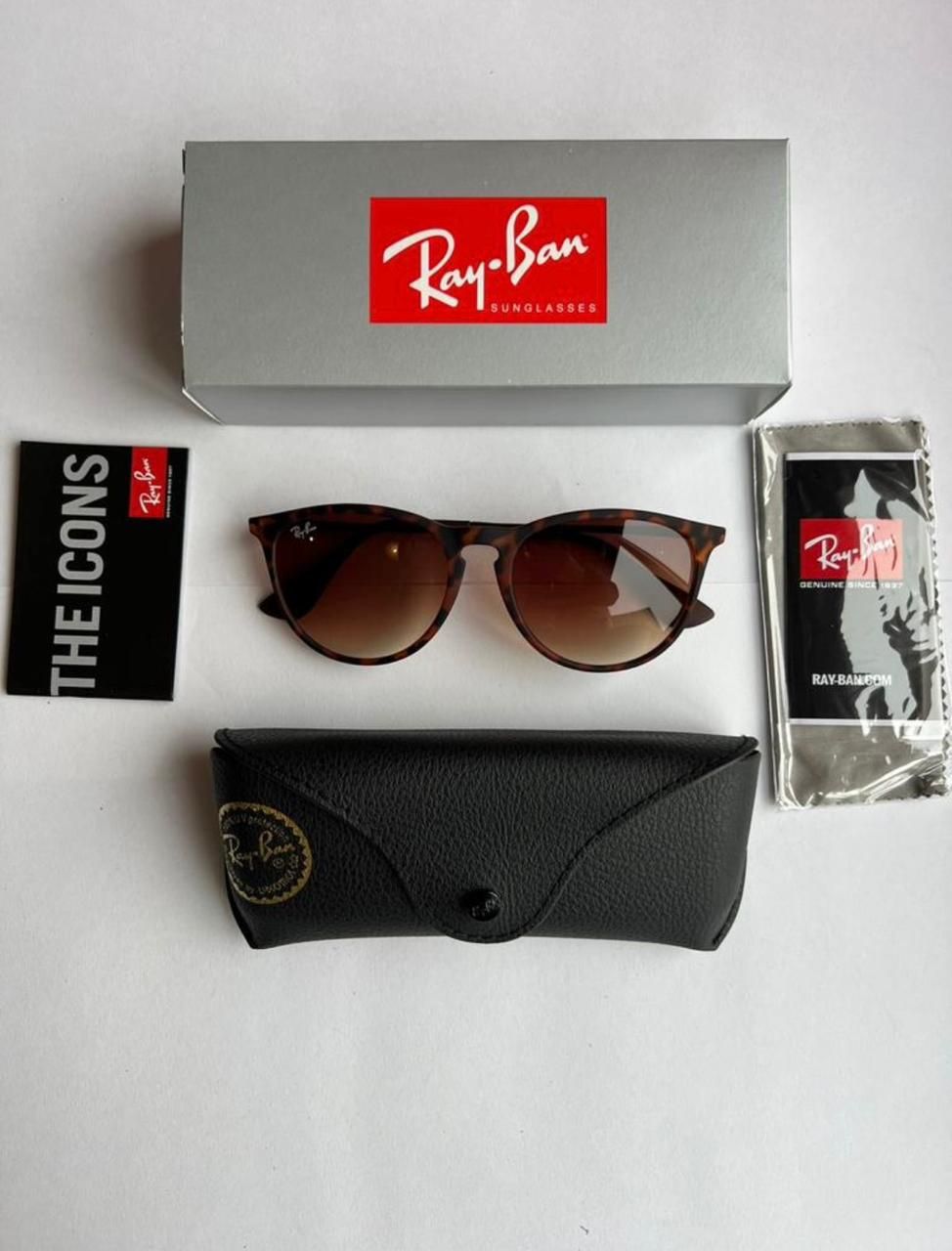 Gafas de sol Ray-Ban, estuche, caja y paño de limpieza sobre una superficie blanca. Montura marrón y lentes degradadas.