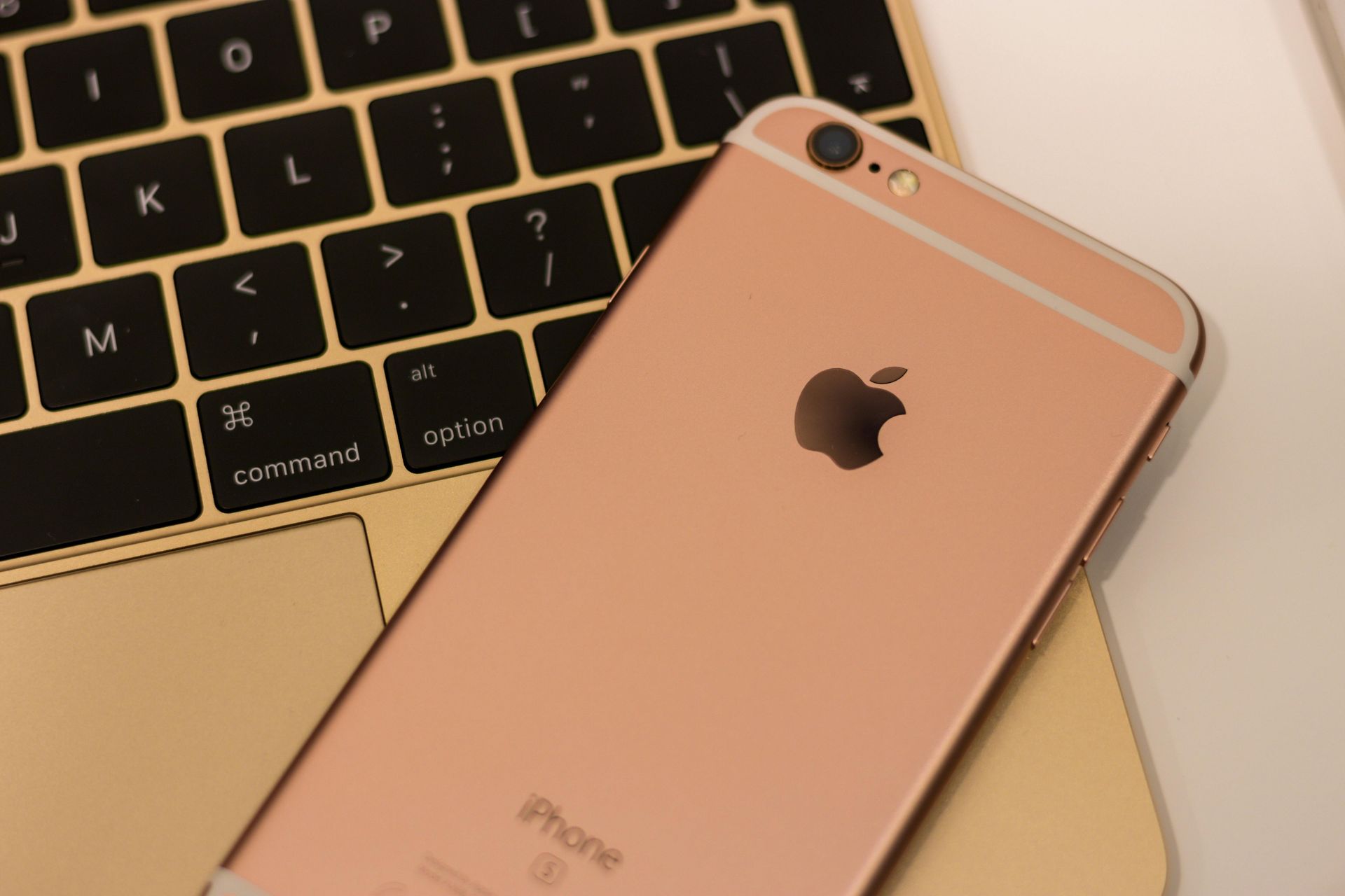 IPhone de oro rosa sobre un teclado de computadora portátil, con el logotipo de Apple visible.