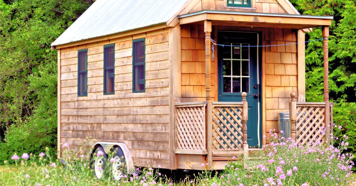 The exterior of a tiny home on wheels. The home has wood siding, a dark-colored front door.