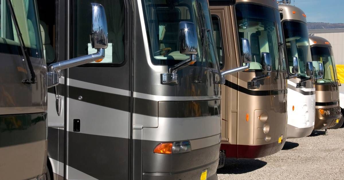 A row of five large recreational vehicles parked next to each other on a sunny day. Each vehicle is a different color.