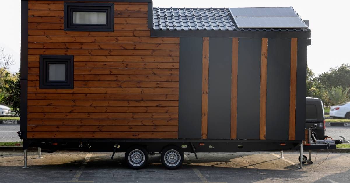 A side view of a tiny home with wood siding and solar panels on the roof.