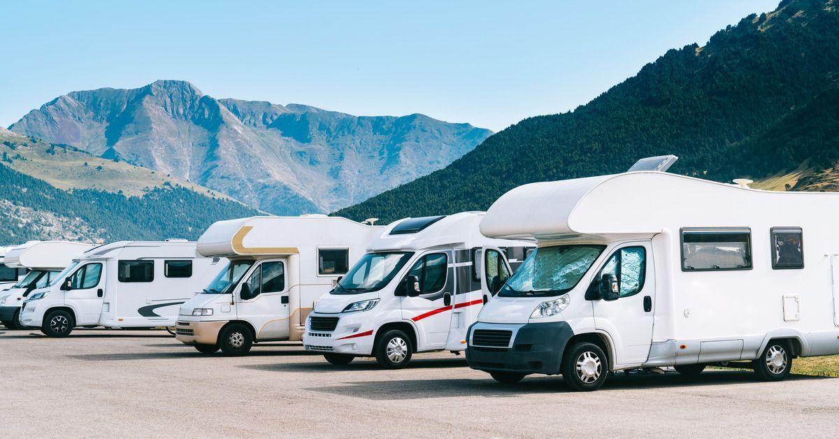 Several white RVs parked next to each other. There are large mountains behind the vehicles.