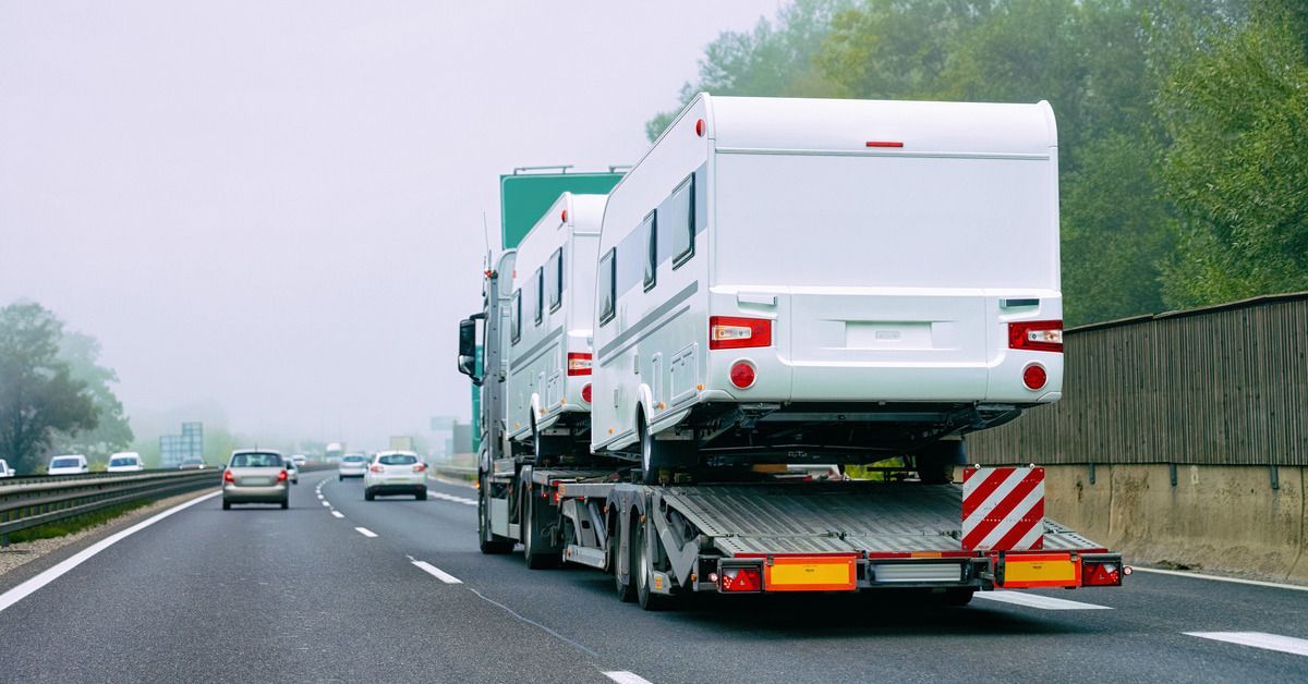 A semi truck with a green cab transporting two white RVs along a multi-lane roadway.