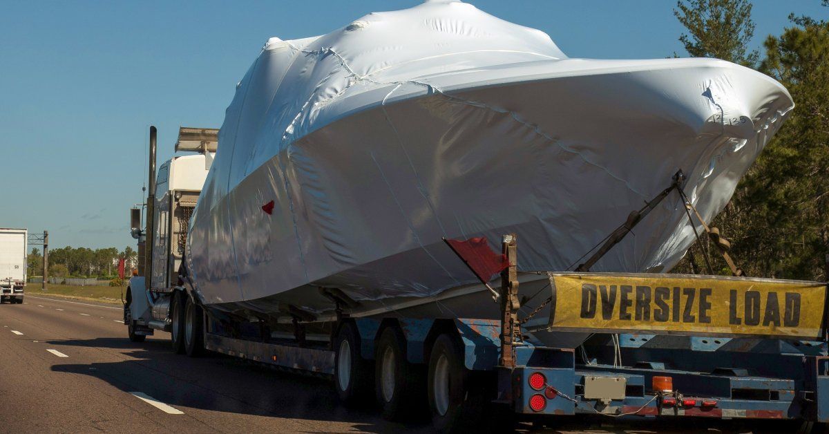 A truck transporting a boat in a white cover. The truck has a yellow sign that says 