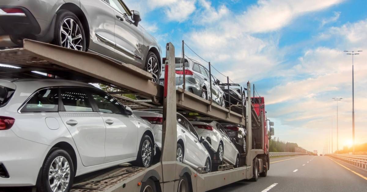 A semi-truck hauling cars on a long trailer with two levels. The truck is driving on a highway.