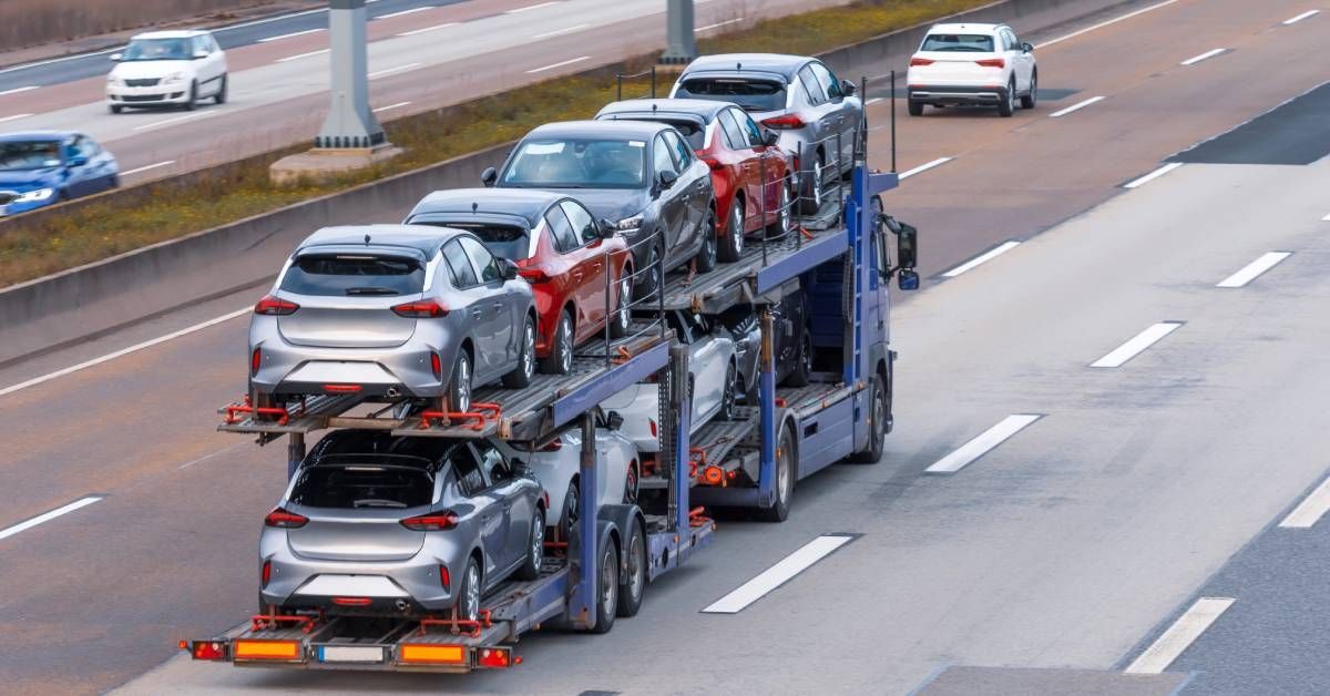 A blue semi-truck hauling several vehicles on its trailer. The truck is driving on a highway.