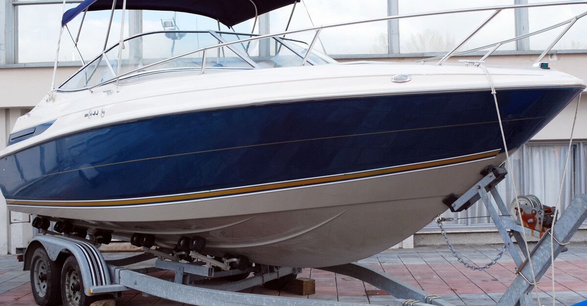 A blue and white motorboat secured to a metal trailer. The trailer is in a room with many windows.