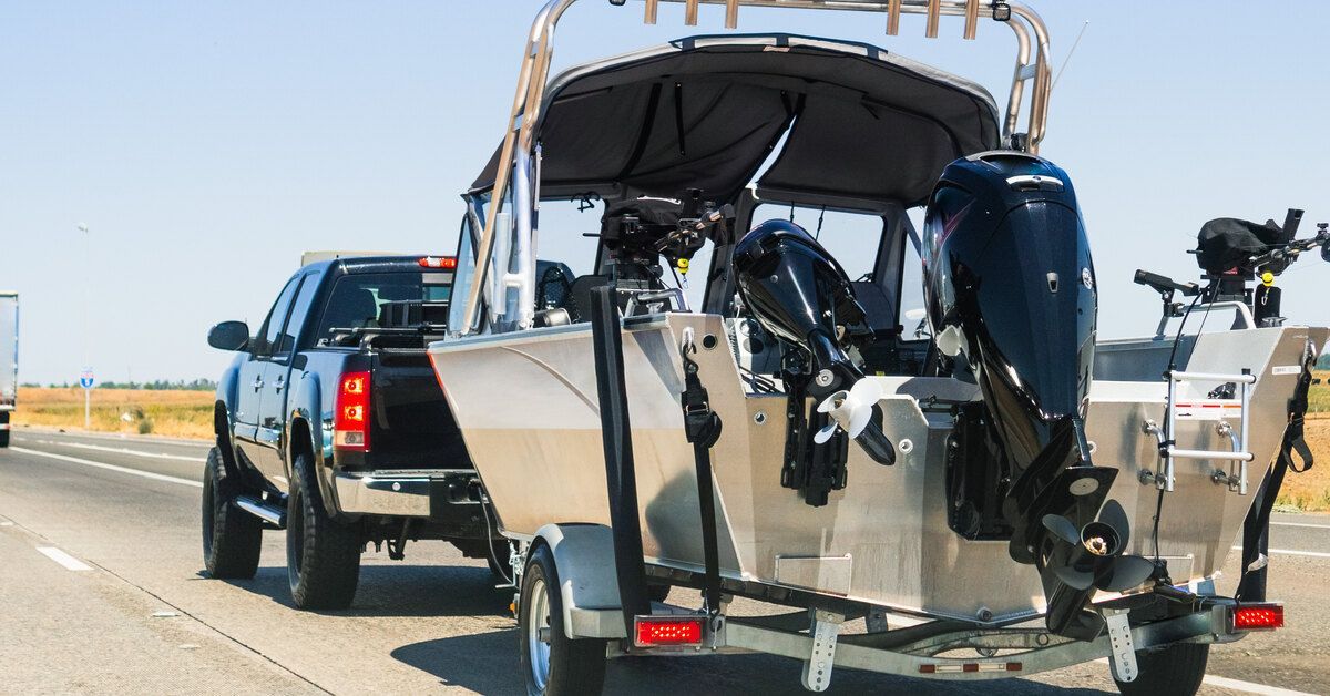 A black pickup truck hauling a silver boat. The truck is driving down a highway on a sunny day.