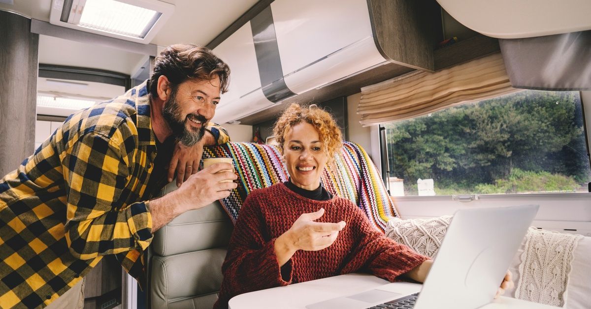 A man wearing a plaid shirt and a woman wearing a red sweater looking at an open laptop inside an RV