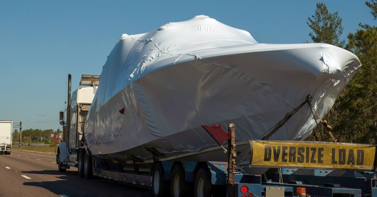 A truck hauling a large boat wrapped in a white covering. The back of the truck has a yellow