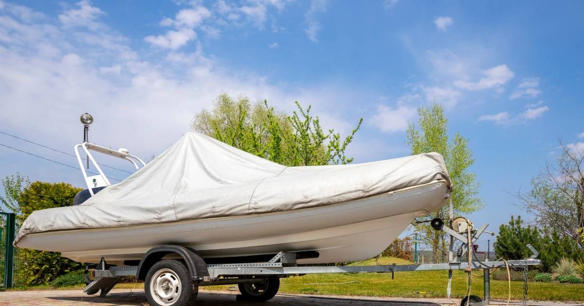 A white motorboat covered with a white protective tarp on a steel trailer with a blue sky in the bac