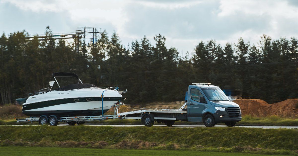A truck with a blue cab towing a black and white motorboat on a trailer with trees in the background.