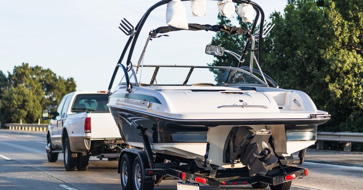 A pickup truck towing a white and black boat with a single engine on a highway surrounded by trees.