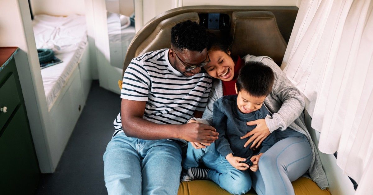 A happy multiracial family of three cuddles on a pull-out bed in their small RV or van mobile home.