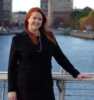 A woman in a black suit is standing on a bridge overlooking a body of water.