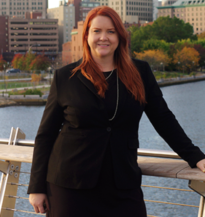 A woman in a black jacket stands on a bridge overlooking a body of water